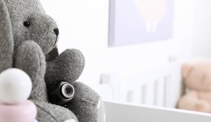 A small black hidden camera tucked into a grey stuffed animal